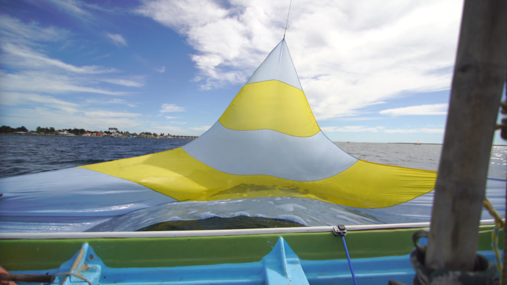 The big sail is constantly raised and lowered. On our sailboat, the sails only rarely touch the water. But for Alfonso’s rig, he uses the water to ‘shorten’ sail, letting his sail rest in the water when the winds gust stronger. Photo from video by Jon Neely.