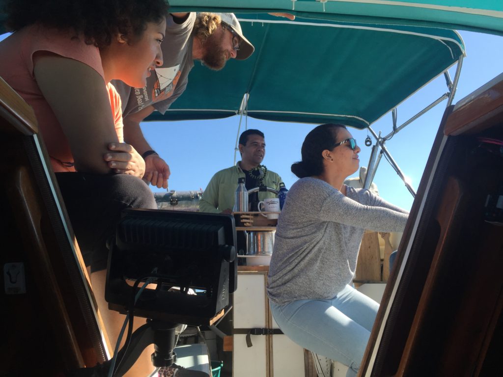 Martin at the helm of Oleada while Josh and one of his students cheer on another student wrapping the jib sheet around a winch.